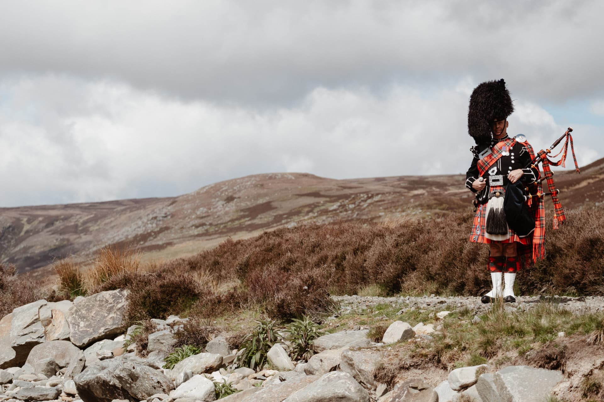 Neil Ironside in full Highland dress with bagpipes on a Scottish moor
